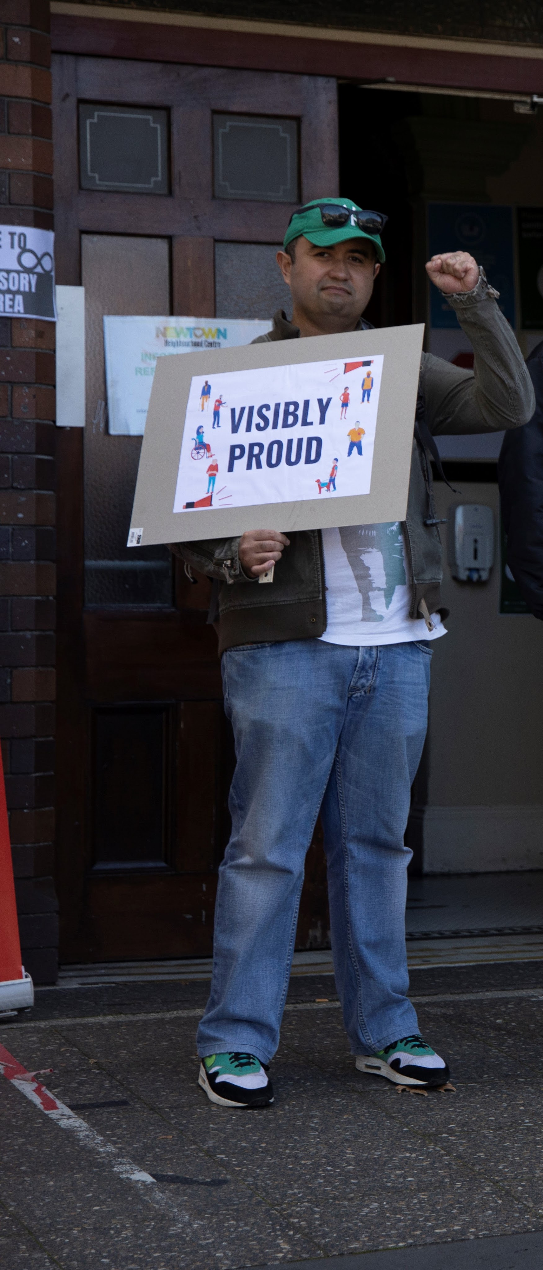 Man pumping the air with his fist, holding a sign that says, "visibly proud" 