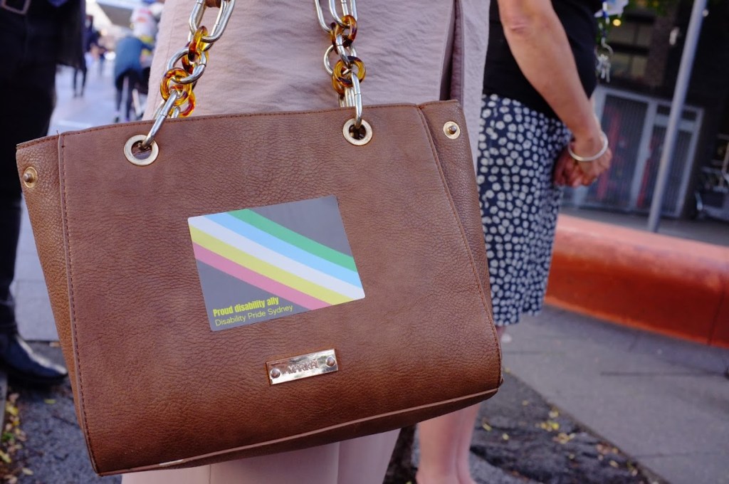 a bag with a sticker on it. The sticker has the disability pride flag and the words "Proud Disability Ally: Disability Pride Sydney" 