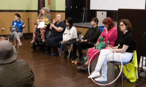 Our panel of 4 disabled people, one speaking into a microphone, an Auslan interpreter and our host, who is a wheelchair user.